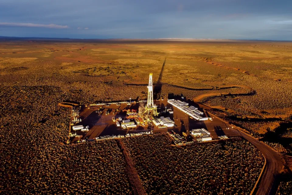 Aerial view of fracking equipment in desert-type plain at golden hour.